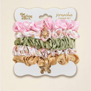 Set of scrunchies with charms on a branded card, featuring pink, green, and gold colors.