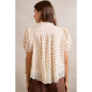 Woman wearing a beige blouse with brown polka dots against a neutral background