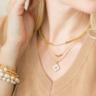 Woman wearing a gold necklace with a floral pendant and pearl bracelets on a neutral background