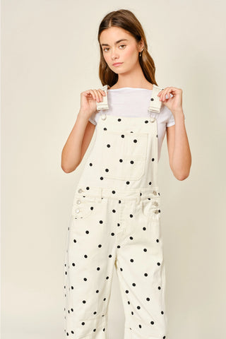 Woman wearing a white polka dot jumpsuit against a beige background