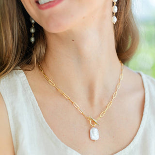 Woman wearing a gold necklace with a pendant, earrings, and a white top.