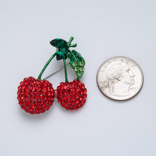Decorative red cherries brooch next to a quarter on a light gray background