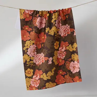 A gathered curtain panel with a dense floral pattern in pink, orange, yellow, and red on a dark brown background, hanging from a thin cord against a light gray wall.