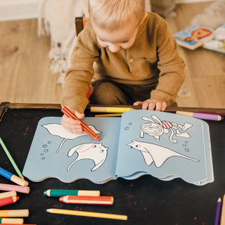 Child coloring a book with crayons on a wooden floor.