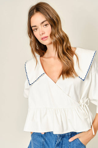 Woman wearing a white blouse with blue trim against a plain background
