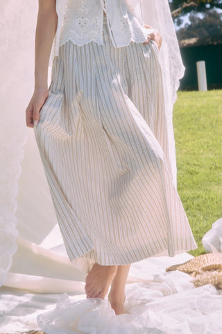 Person wearing a white lace top and striped skirt standing outdoors with grass and a blurred background.