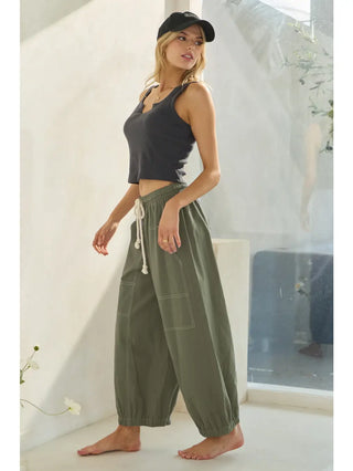 Woman wearing a black tank top and green wide-leg pants in a bright room.