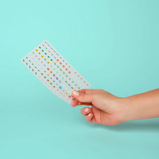 Hand holding a clear sheet with colorful stickers against a light blue background
