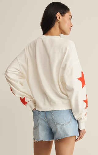 Person wearing a white sweatshirt with red star patterns and denim shorts on a neutral background