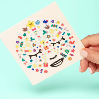 Sheet of colorful emoji-style stickers held by a hand against a light blue background