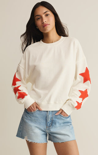 Woman wearing a white sweater with red star patterns and denim shorts on a plain background