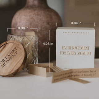 A boxed candle set labeled 'ENCOURAGEMENT FOR EVERY MOMENT' by Sweet Water Decor, shown with a white box, wooden lid, glass vessel, and small prayer cards on a tabletop. Measurement callouts indicate 3.