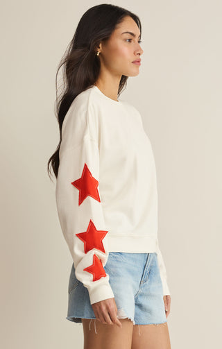 Woman wearing a white sweater with red stars and denim shorts on a beige background