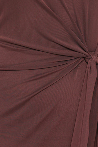 Close-up of a draped fabric garment in a dusty rose or mauve color, showing the texture and a twisted knot detail on the right side.