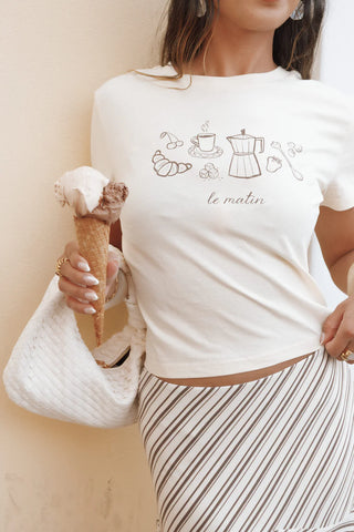 Woman wearing a white t-shirt with coffee-themed graphics and text, holding an ice cream.