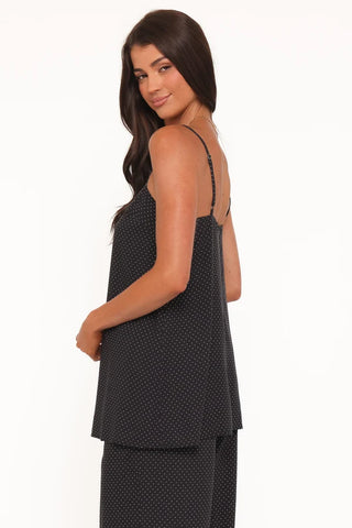 A woman modeling a black camisole top with a small white polka dot pattern, shown from a side-back angle against a plain white background.