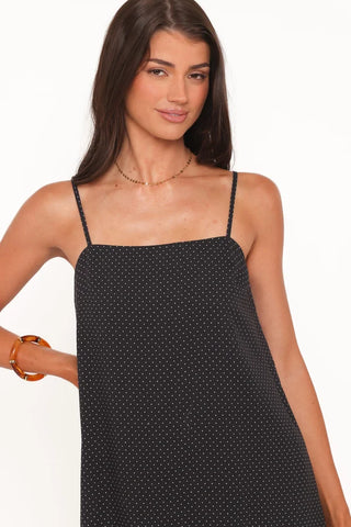 A woman wearing a black spaghetti-strap camisole dress with a small white polka dot pattern, shown against a plain white background.