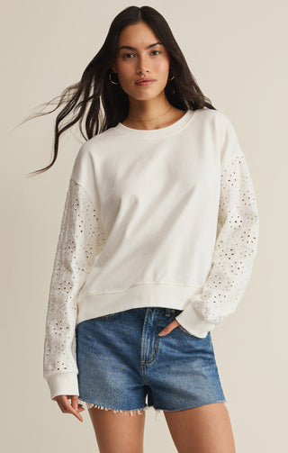 Woman wearing a white sweatshirt with sheer sleeves and denim shorts on a beige background