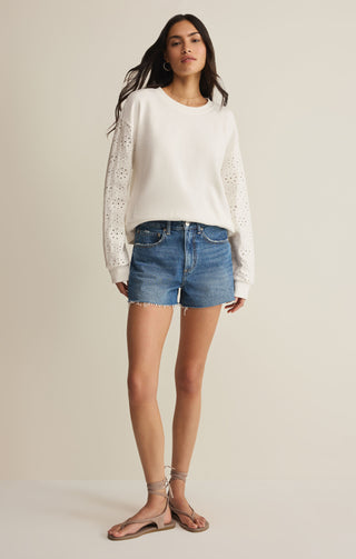woman wearing long sleeve white tee shirt and denim shorts on beige background