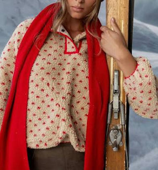 Person wearing a patterned jacket with a red scarf holding skis against a snowy background