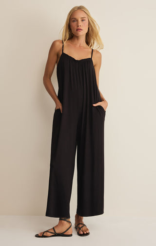 Woman wearing a black jumpsuit against a beige background