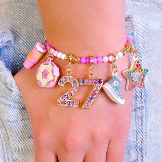 A close-up of a person's wrist and hand wearing a colorful beaded bracelet with soccer-themed charms, including a soccer ball, a star, a shoe, and a number 27 charm.