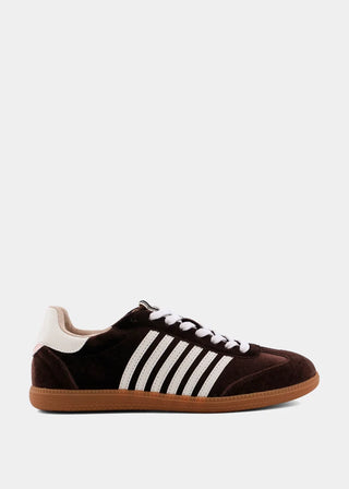A dark brown suede sneaker with three white stripes on the side, white laces, a cream heel tab, and a gum brown sole, shown against a plain light gray background.
