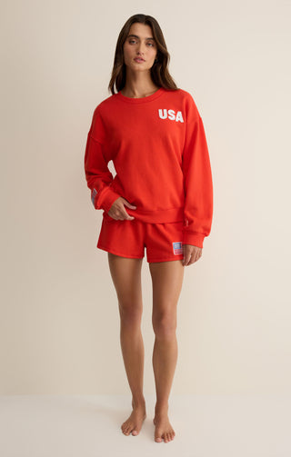 Person wearing a red 'USA' sweatshirt and shorts on a beige background
