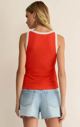 Woman wearing a red sleeveless top with lace trim and denim shorts on a beige background