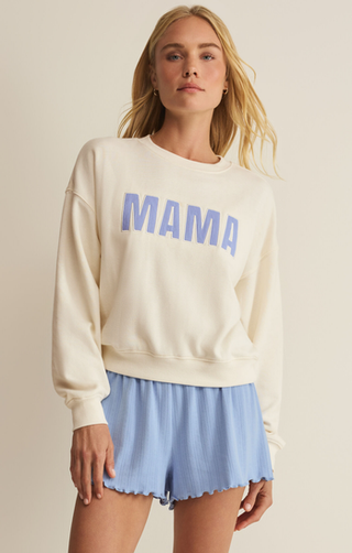 Woman wearing a cream sweatshirt with 'MAMA' in blue and light blue shorts on a beige background