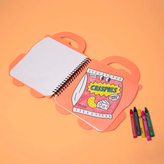 Notebook with a colorful cereal box design on an orange background, accompanied by crayons.